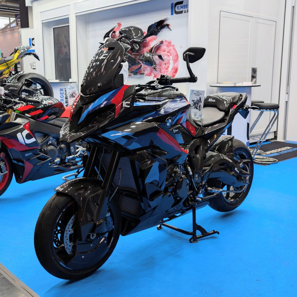 BMW M 1000 XR Motorrad aus Carbon in Blau und Rot auf blauem Messeboden am Stand von Ilmberger Carbon Parts.