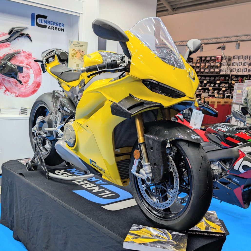 Gelbe Ducati Panigale mit Carbon-Komponenten am Messestand von Ilmberger Carbon auf einem schwarzen Podest.