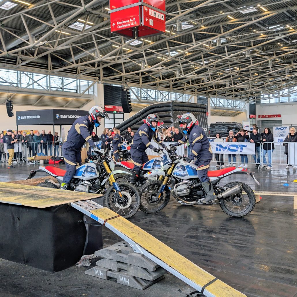 Drei Stuntfahrer auf BMW R 12 G/S Motorrädern führen auf der IMOT Messe eine synchronisierte Show vor Publikum vor.