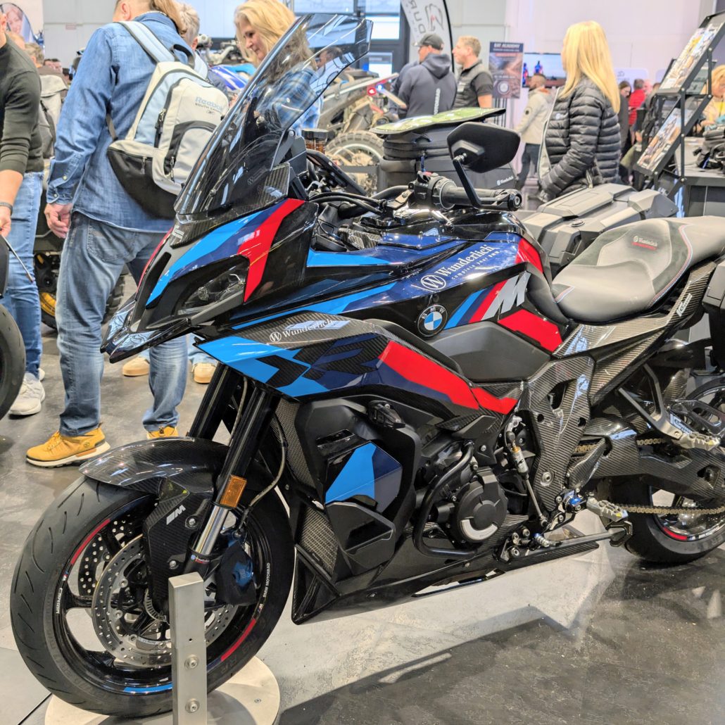 Wunderlich BMW S 1000 XR Performance Motorrad mit Carbon-Teilen und M-Farben auf einer Messe mit Publikum.