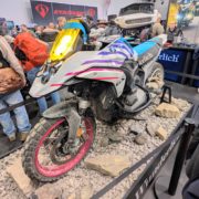 Wunderlich BMW R 1250 GS mit gelbem Scheinwerfer, pinken Felgen und Offroad-Bereifung auf Steinen am Messestand.