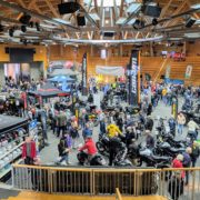 Übersicht einer Motorradmesse in einer großen Halle mit vielen Besuchern, Motorrädern, Ständen und Can-Am Werbebannern.