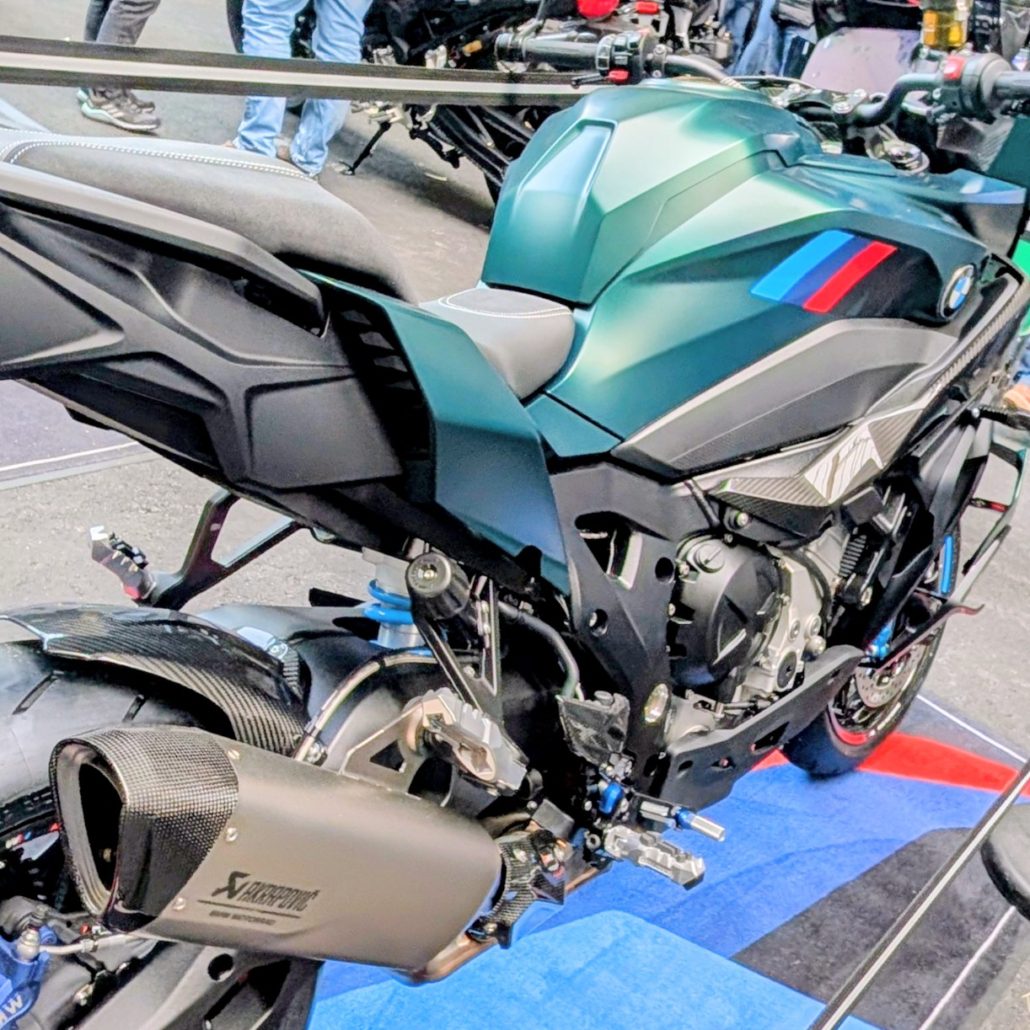 Grünes BMW M 1000 R Motorrad mit Akrapovič-Auspuff, Carbon-Details und M-Farben auf einer blau-roten Ausstellungsfläche.