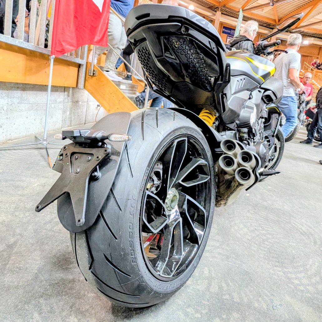 Heckansicht einer Ducati Diavel V4 mit breitem Hinterreifen, schwarzer Alufelge und markantem Vierrohr-Auspuffdesign.