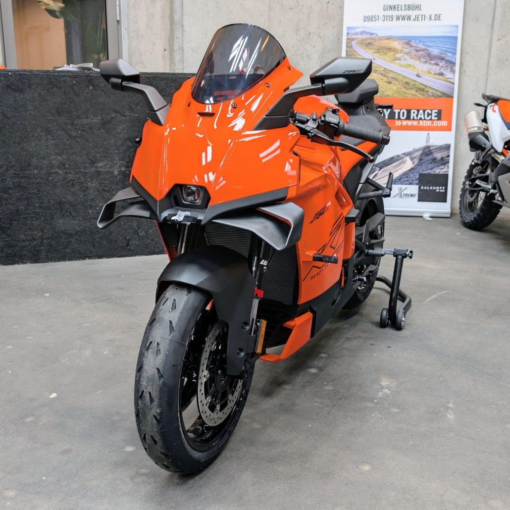 Frontansicht einer orangefarbenen KTM RC Sportmaschine mit Aerodynamik-Wings und „Ready to Race“-Schriftzug auf einem Ständer.