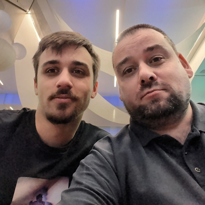 Zwei Männer mit Bart machen ein Selfie in modern beleuchteter Location.