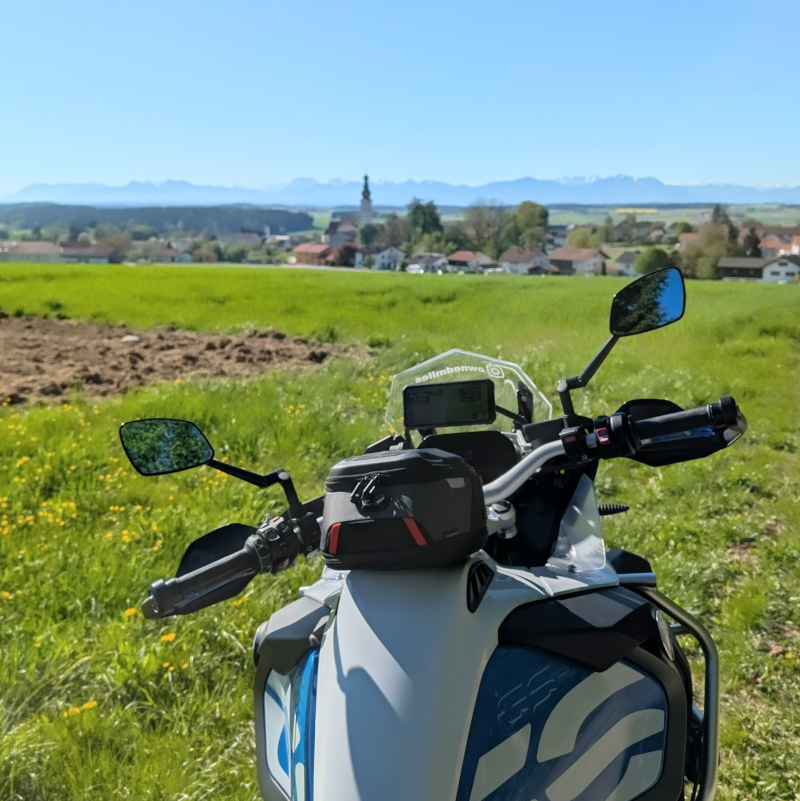 Cockpit der BMW R1200GS mit Tankrucksack und Blick über Felder auf die Berge. Auf dem Windschild steht @ownedmiles.