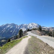Blick über die Rossfeld Panoramastraße auf verschneite Alpengipfel unter strahlend blauem Himmel.