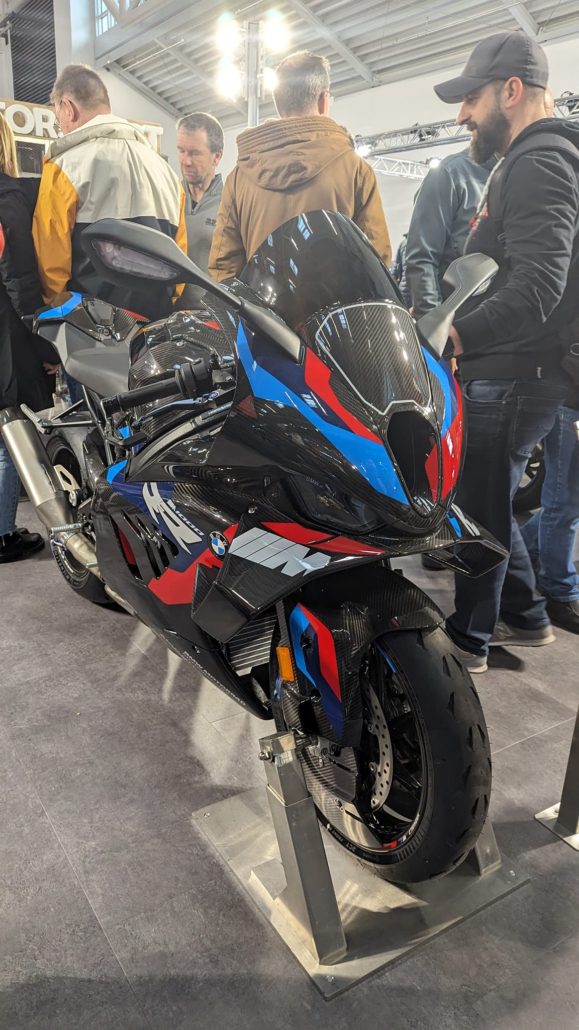 Glänzendes BMW M 1000 RR Supersport-Motorrad mit Carbon-Verkleidung in Schwarz, Blau und Rot auf einem Messestand.