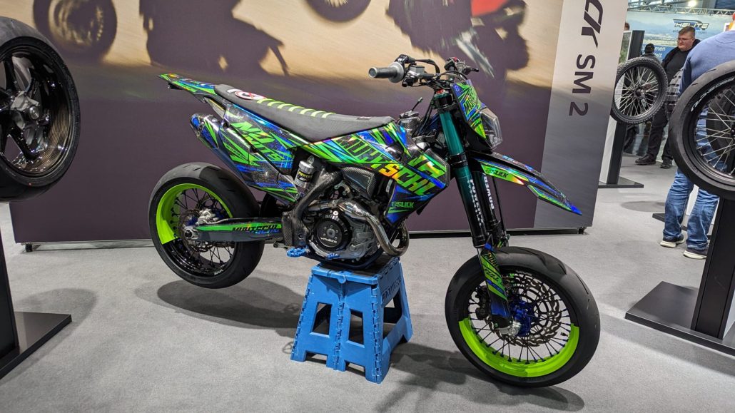 Supermoto-Motorrad mit auffälligem grün-blauem Design; schwarze Felgen, teils neongrün.