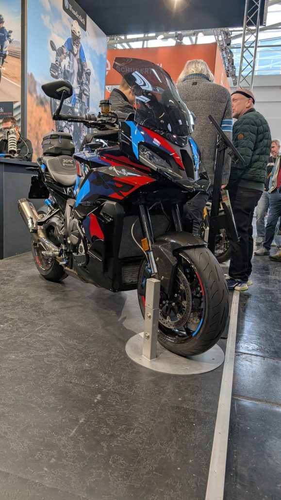 Schwarzes BMW S 1000 XR Motorrad mit blauen und roten Akzenten sowie Carbon-Verkleidung auf einem Messestand.