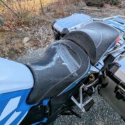 Gefrorene, schwarze Sitzbank eines Motorrads mit blauen und weißen Akzenten, rechts silberne Koffer.