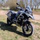 Silber-schwarzes BMW R 1200 GS Adventure Motorrad mit Sturzbügeln und Windschutzscheibe, geparkt auf einer Lichtung am Waldrand.