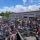 Ein großes Motorradtreffen mit hunderten Motorrädern und Fahrern auf einem gepflasterten Gelände zwischen Lagerhallen.