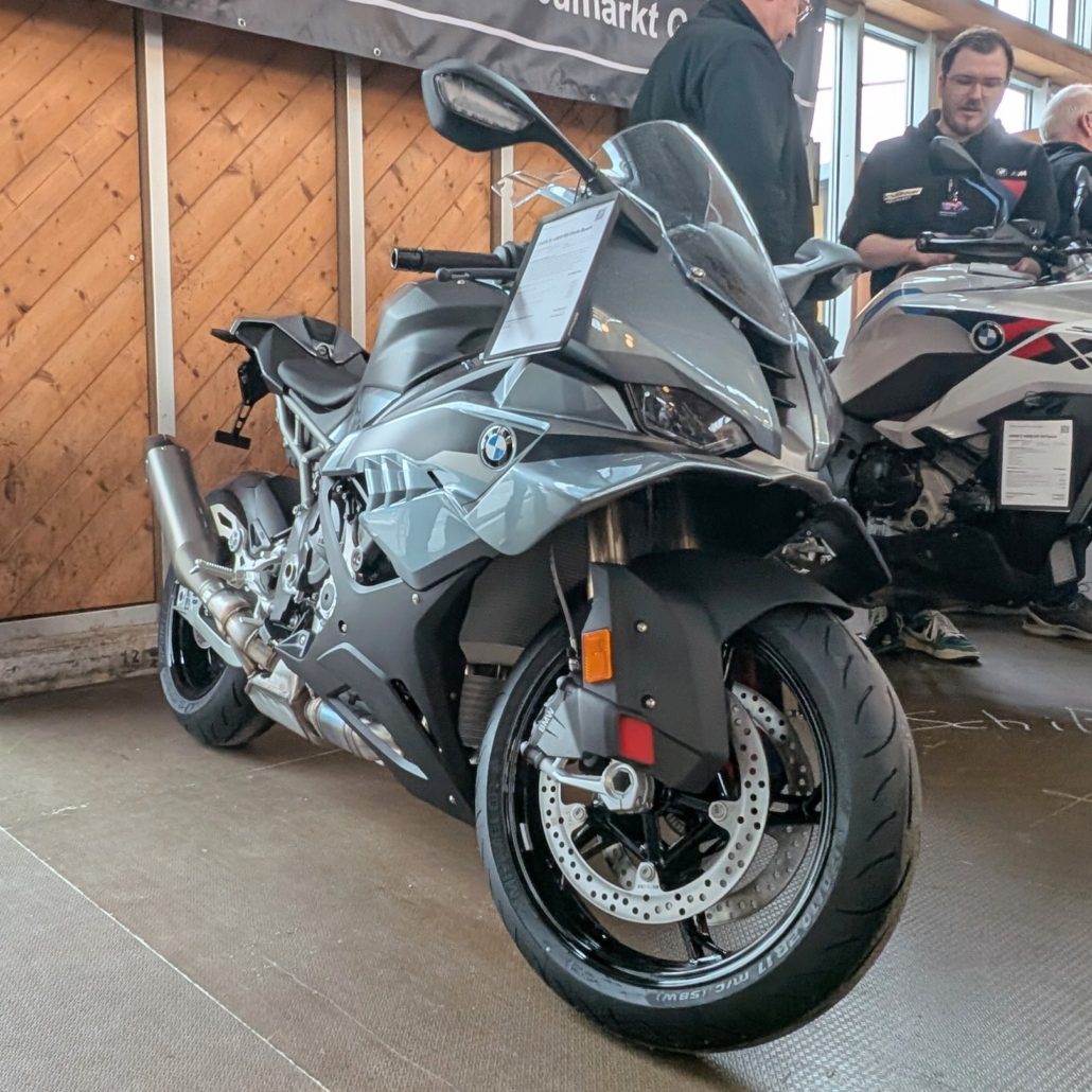 Graues BMW Sportmotorrad mit Metall-Auspuff und schwarzen Felgen steht vor einer Holzwand im Verkaufsraum.