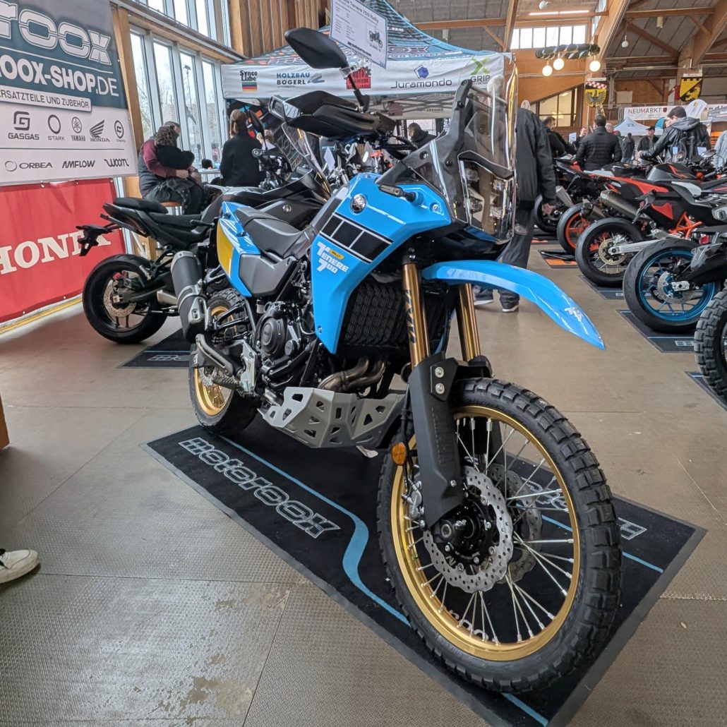 Yamaha Ténéré 700 World Rally in Blau-Schwarz mit goldenen Felgen und Stollenreifen auf einer Motorradmesse.