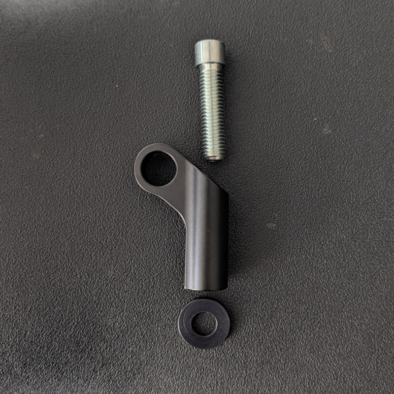 Schwarzes L-förmiges Metallteil, silberne Schraube und schwarzer Gummiring auf dunklem, strukturiertem Untergrund.