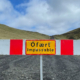 Rot-weiße Straßensperre mit Schild "Ófært Impassable" auf Schotterweg vor grüner Hügellandschaft.