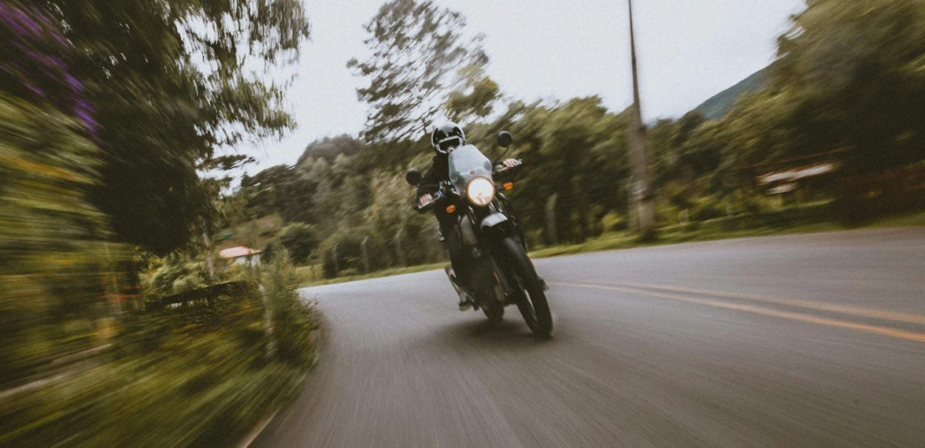 Motorradfahrer auf dunklem Bike in schneller Kurvenfahrt auf einer Waldstraße mit starker Bewegungsunschärfe.