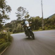 Motorradfahrer auf dunklem Bike in schneller Kurvenfahrt auf einer Waldstraße mit starker Bewegungsunschärfe.