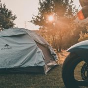 banner-camping-featured Ein graues Zelt steht im Wald, mit Sonnenstrahlen und einem Motorrad-Schutzblech rechts
