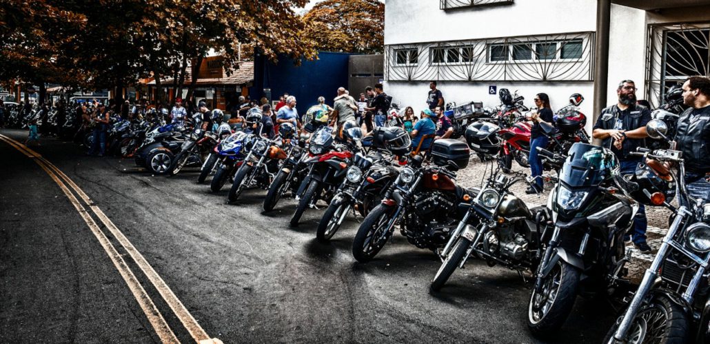 Lange Reihe geparkter Motorräder am Straßenrand und stehende Biker-Gruppen vor einem Gebäude bei einem Treffen.