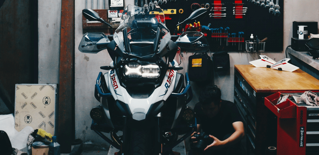 Mechaniker schraubt in gut ausgestatteter Motorradwerkstatt am Vorderrad einer frontal stehenden BMW R1200GS.