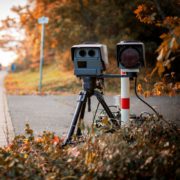 Tragbarer PoliScan-Blitzer auf Stativ am herbstlichen Rand einer leeren Landstraße zur Kontrolle des Tempolimits für Motorrad.