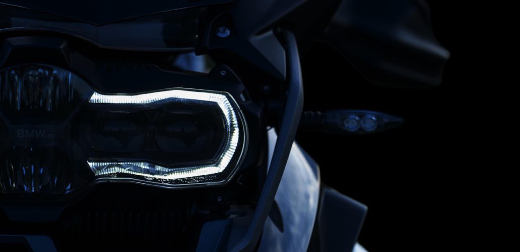 Nahaufnahme des leuchtenden, u-förmigen LED-Tagfahrlichts (BMW LED) eines Motorrad-Scheinwerfers bei Dunkelheit.