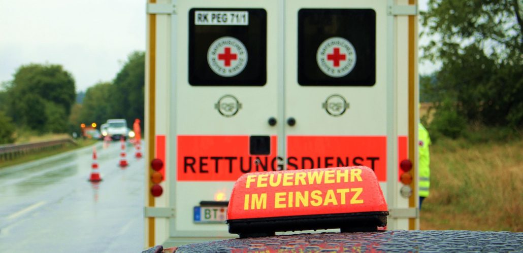 Rückansicht eines Rettungswagens bei Regen. Davor ist ein Schild mit der Aufschrift Feuerwehr im Einsatz