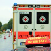 Rückansicht eines Rettungswagens bei Regen. Davor ist ein Schild mit der Aufschrift Feuerwehr im Einsatz