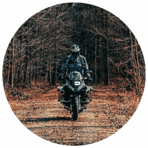 Ein Motorradfahrer in voller Ausrüstung fährt auf einem Waldweg durch einen kahlen, dunklen Wald