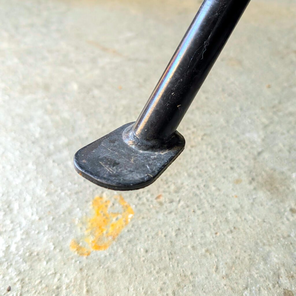 Schwarzer Motorrad-Seitenständer aus Metall ohne montierte Verbreiterung vor hellem Betonboden.