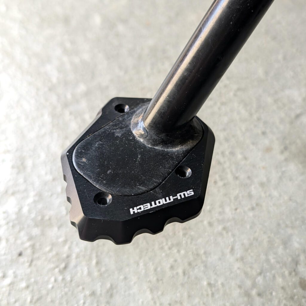 Schwarzer Motorrad-Seitenständer mit montierter SW-MOTECH Verbreiterung aus gefrästem Aluminium vor Betonboden.