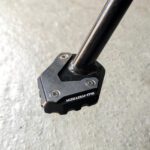 Schwarz-silberne SW-MOTECH Seitenständer-Fußverbreiterung aus Aluminium und Edelstahl an einem schwarzen Motorradständer.