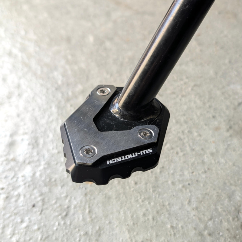 Schwarz-silberne SW-MOTECH Seitenständer-Fußverbreiterung aus Aluminium und Edelstahl an einem schwarzen Motorradständer.